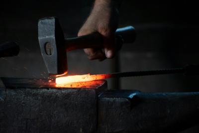 Klensmed slår med metallhammare på glödande metall ovanpå ett städ